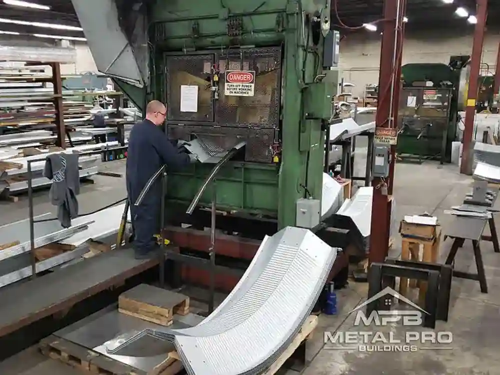 Worker operating industrial press forming curved steel panels at MPB Metal Pro Buildings.