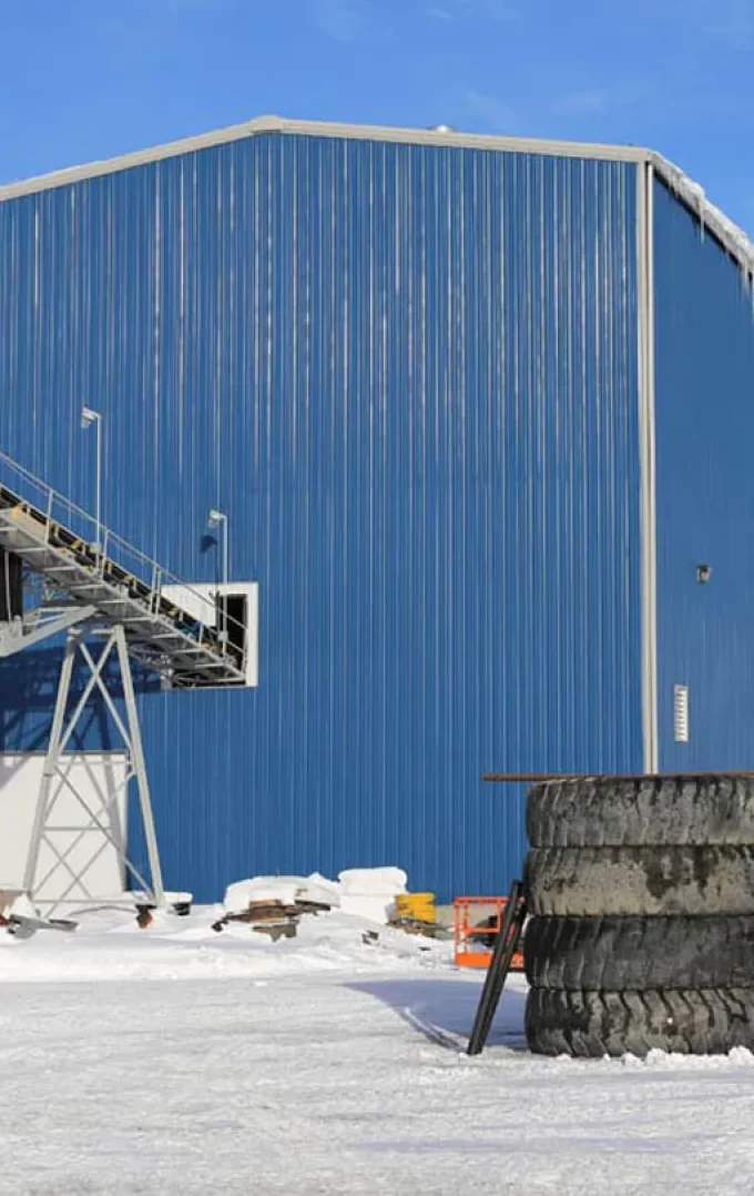 Large blue steel industrial building in snowy area with conveyor system and stacked tires.