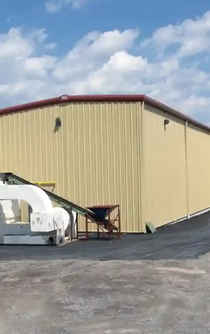 Large tan industrial steel building with red trim, equipment outside, and clear blue sky.